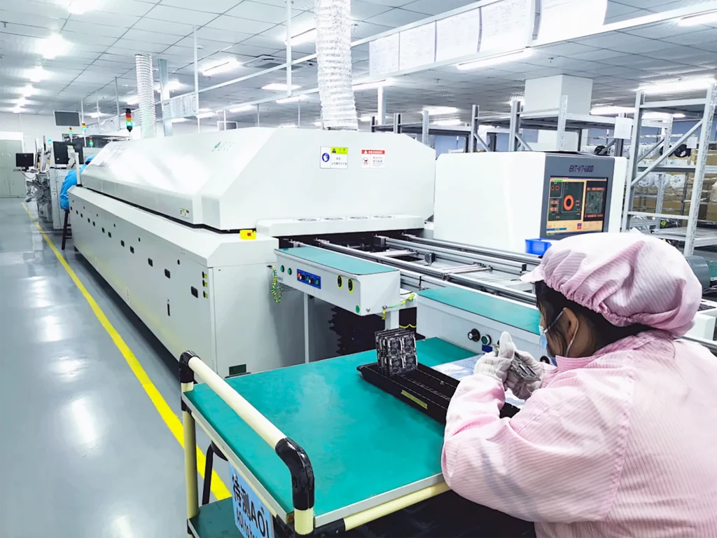 Operator seated at reflow soldering line inspecting LED boards after oven