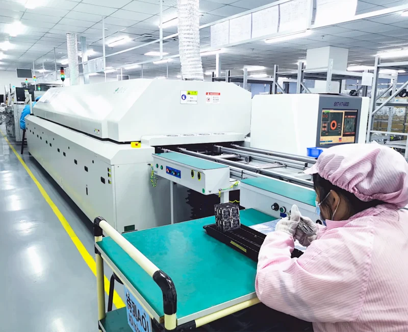 Operator seated at reflow soldering line inspecting LED boards after oven